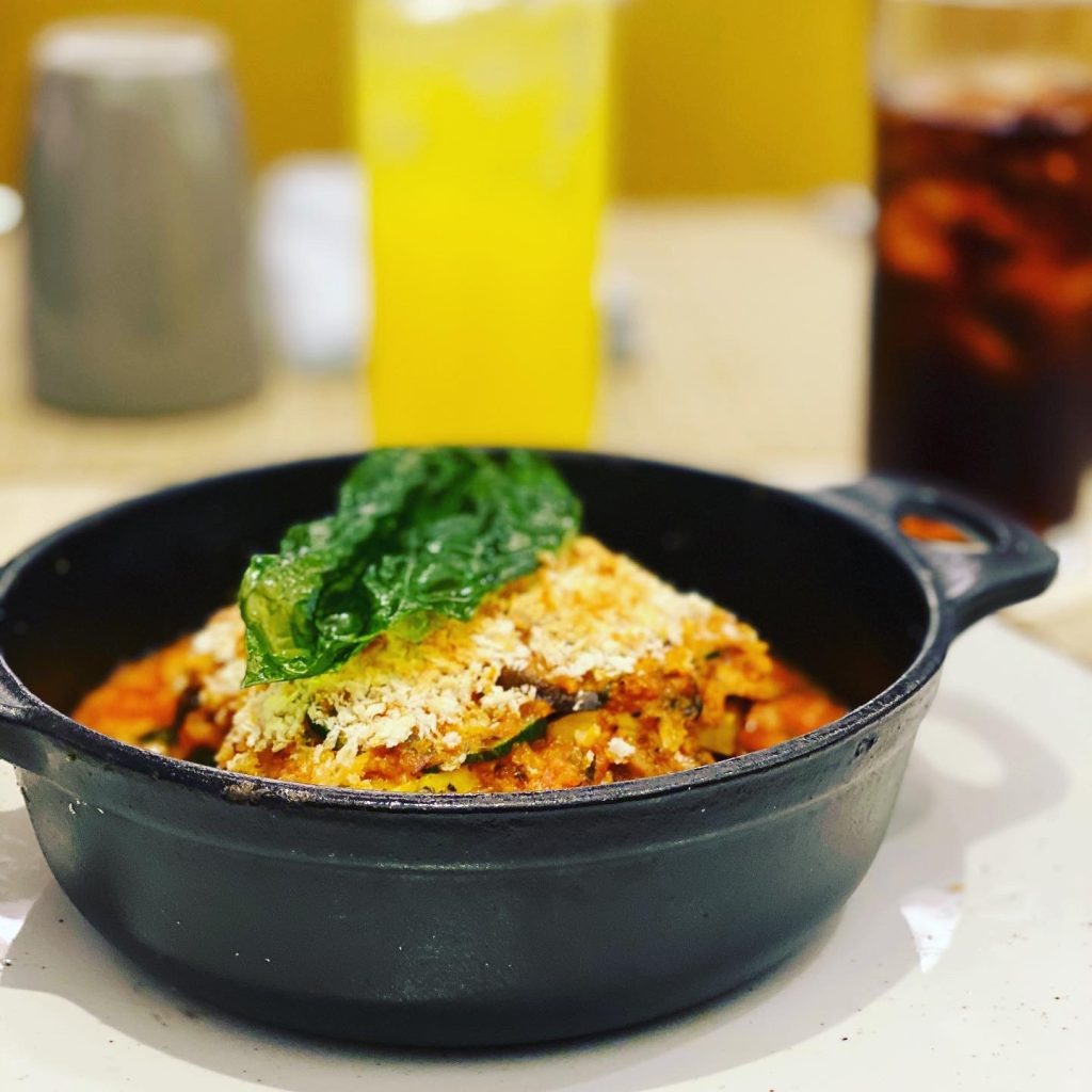Vegetable bake with tomato sauce and zucchini, topped with breadcrumbs and a large green leaf in a black skillet