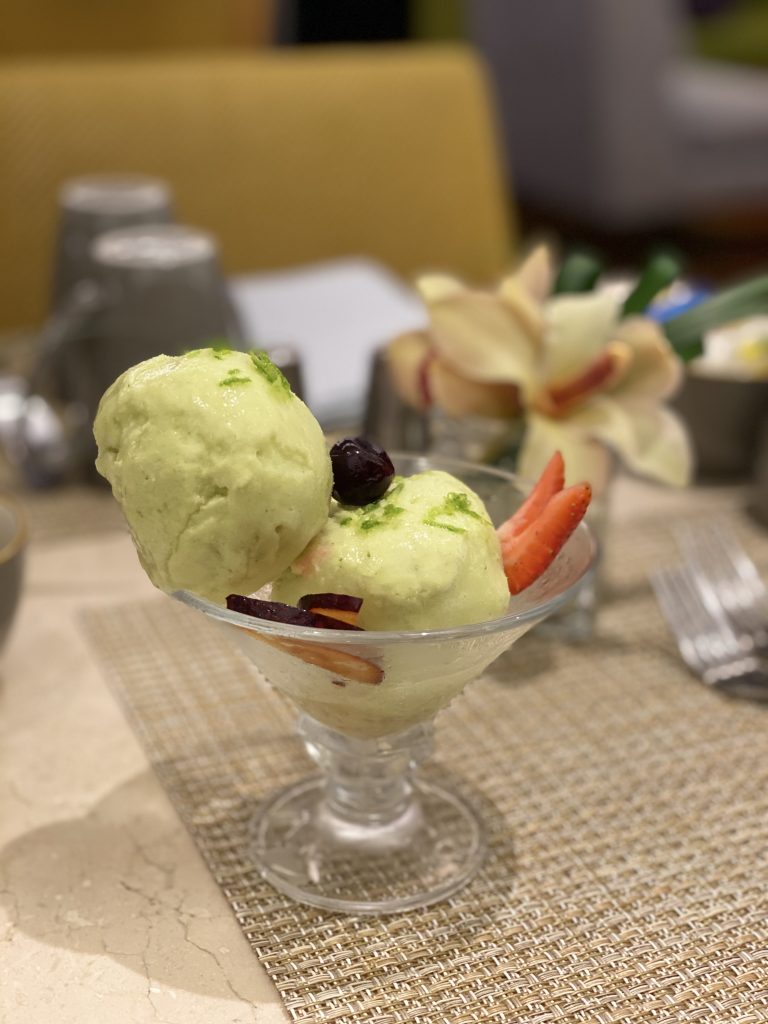 Two scoops of light green sorbet topped with lime zest, strawberry slices, and a cherry in a glass dish